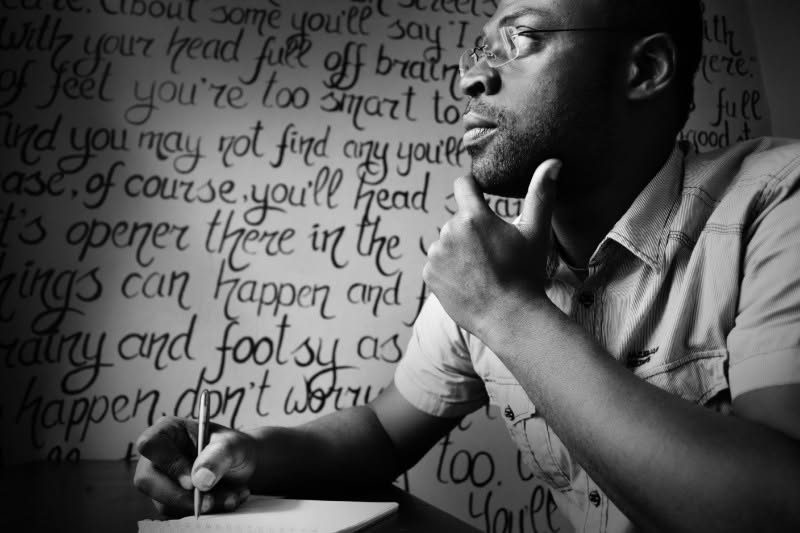 Jay C. Patsson writing at his desk in front of a wall of handwritten text